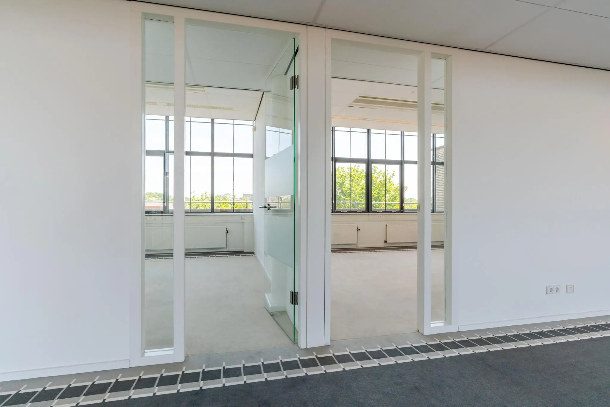 Lichte, lege kantoorruimte aan de Van Alkemadelaan met glazen deuren en grote ramen.